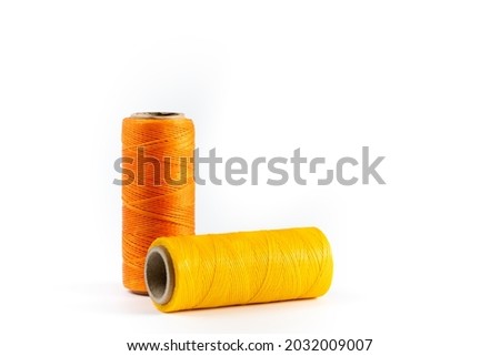 Yellow and orange spools of thread on a white background. Waxed orange and yellow threads for leather products. Yellow thread. Orange thread.