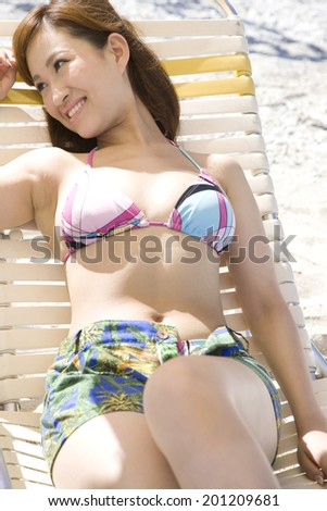 The woman with a swimming suit relaxing to sit on the deck chairs on the beach