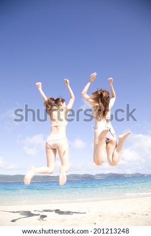 The rear view of two women with a swimming suit jumping on the beach
