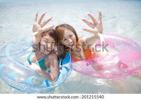 Two women with a swimming suit reaching their hands on floats in the sea