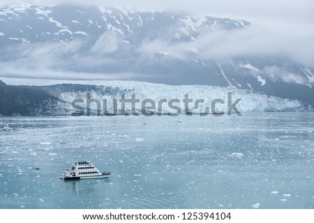 Small boat with tourist approaching Hubbard glacier in Alaska fjord.