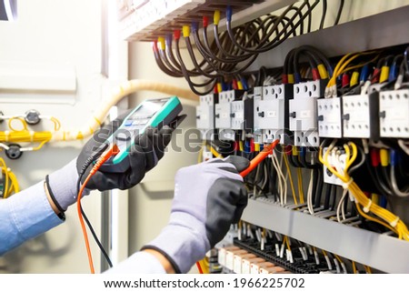 Electrical engineer using digital multi-meter measuring equipment to checking electric current voltage at circuit breaker and cable wiring system in main power distribution board. Foto d'archivio © 