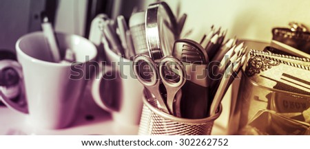Writing instruments in glasses on a shelf.