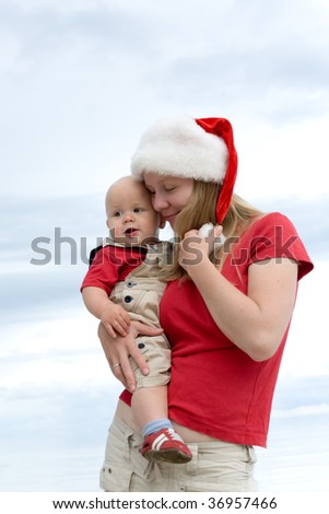 Young attractive mom with Santa\'s hat and the little baby on the cloudy sky background