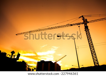Industrial construction cranes and building silhouettes on sunset