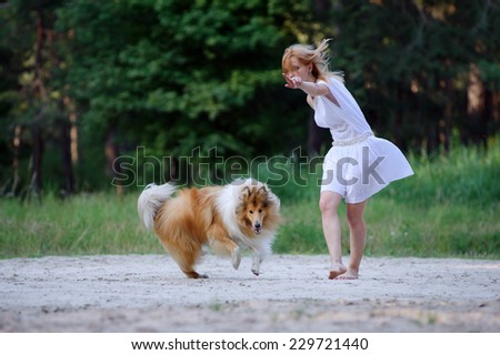 Beautiful young girl in a white dress indicates the camera and her collie dog running on the photographer. Man and dog are engaged in a forest