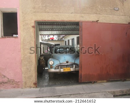 Matanzas, Cuba, August 8, 2012: Old-fashioned cuban car in a garage in Matanzas, Cuba. I like the colour of this image, the red of the door, pink of the wall and blue of the car.