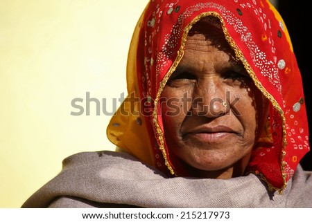 Pushkar, India, November 28, 2012: Old Indian woman looking straight at the camera. She worn a typical Indian veil, red and yellow, and sha has an earring on the nose.
