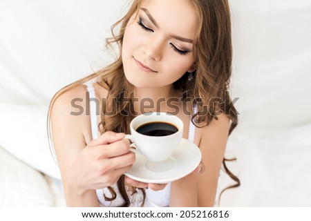 Young brunette woman with a cup of coffee in bed at home in the morning