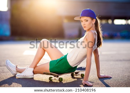 Closeup summer portrait of pretty young woman posing in urban, hipster girl with skate board in town. Summer evening sunlight