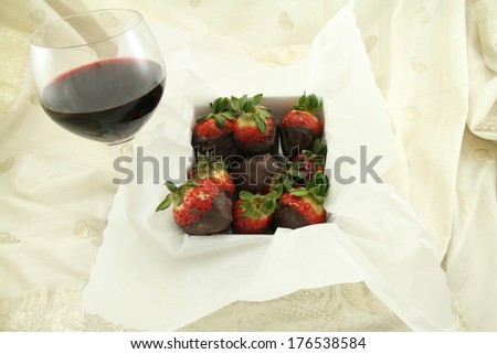 A glass of red wine and box of chocolate strawberries.