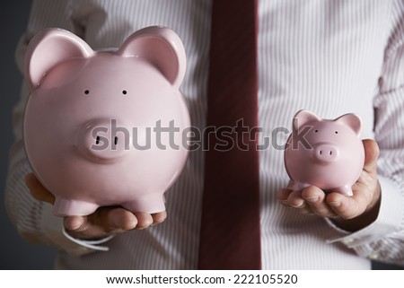 Businessman Holding Large And Small Piggy Bank