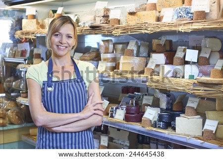 Owner Of Delicatessen Standing Next To Cheese Display