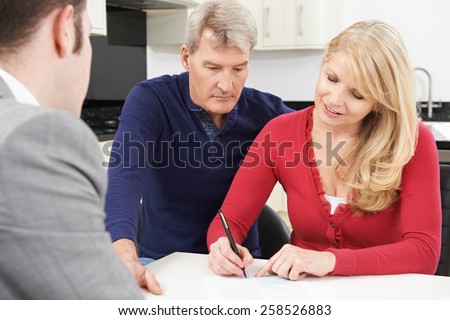 Mature Couple With Financial Adviser Signing Document At Home