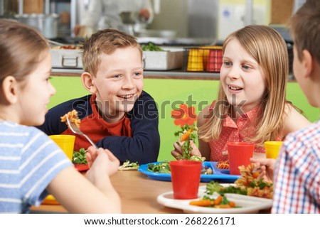 Group Of Pupils Sitting At Table In School Cafeteria Eating Lunch