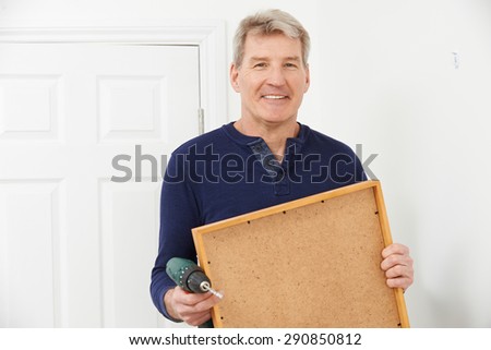 Mature Man Drilling Wall To Hang Picture Frame