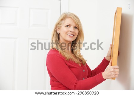 Mature Woman Hanging Picture On Wall