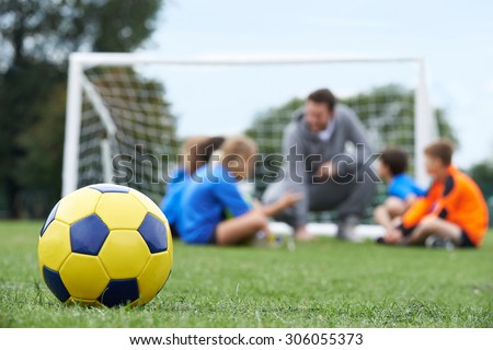 Coach  And Team Discussing Soccer Tactics With Ball In Foreground
