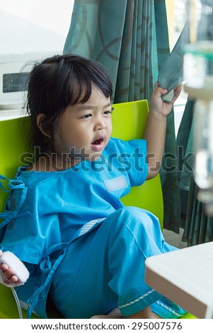 Illness little asian kids sit on a chair in hospital, saline intravenous (IV) on hand