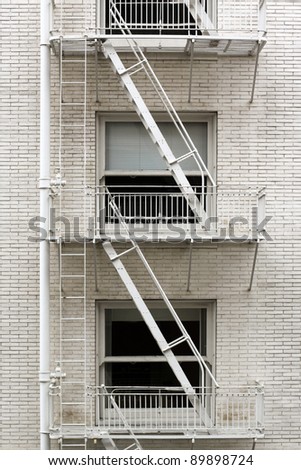 Fire escape ladder zigzagging across the face and windows of a brownstone that\'s been painted white.