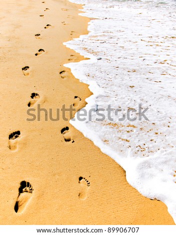 Male and female footsteps imprinted side by side in the sand.