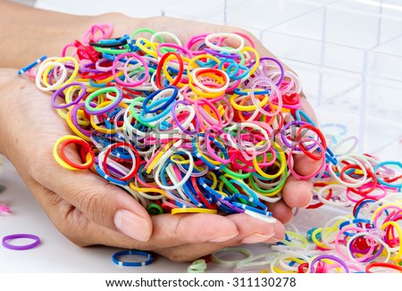 hands and pile of small round colorful rubber bands rainbow color for making rainbow loom bracelets on the table