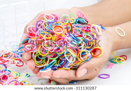 hands and pile of small round colorful rubber bands rainbow color for making rainbow loom bracelets on the table