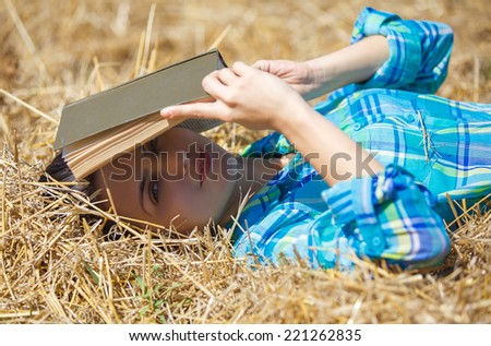 young girl sitting on golden reap wheat in yellow sunset field Woman holding in hands interesting book, reading text