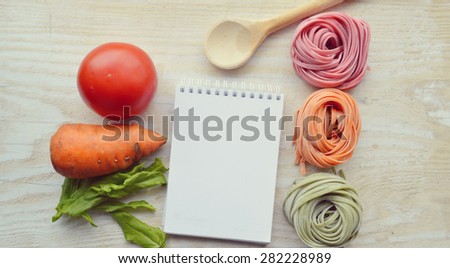 recipe book,vegetables(carrots, spinach, tomato) raw colored pasta.Notepad to write the recipe on the background of pasta.Cooking concept.spaghetti