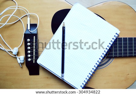 Music recording scene with classical guitar, notebook and headphones on wooden table, closeup
