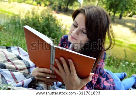 woman sitting on a plaid and reading a book in park