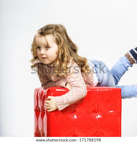 Cute little girl with red cube-chair posing in studio