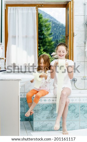 Two sisters playing with toilet paper roll in bathroom