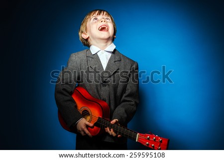 Red-haired preschooler boy with ukalele, isolated on blue, music concept