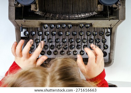 Cute little girl typing letter on vintage typewriter keyboard