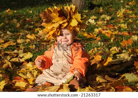 7-months Smiling Baby-girl with maple leaves on head sitting in pile of maple leaves