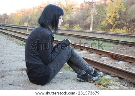 Girl sit between rails and abandon railroad station