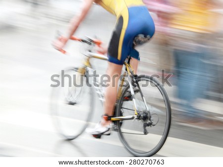 A very fast bicycling man dressed in blue and yellow. The speed makes it un-sharp. Brightly lit.