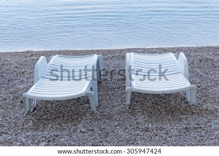 Two white deck chairs on the beach in the first blue morning light before sunrise