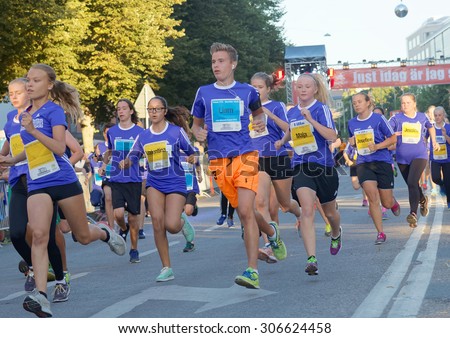 STOCKHOLM, SWEDEN - AUG 15, 2015: Group of 15 year old girls and boys running in a curve in blue dresses during the start of the running event Midnattsloppet, August 15, 2015 in Stockholm, Sweden