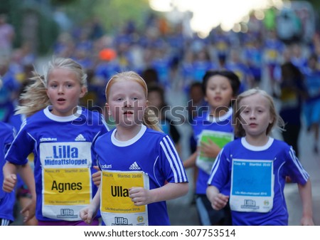 STOCKHOLM, SWEDEN - AUG 15, 2015: Group of young blonde girls running, followed by a large group of competitors in the running event Midnattsloppet, August 15, 2015 in Stockholm, Sweden
