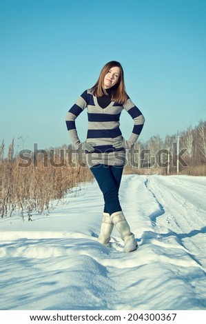 Young brunette girl in stripe sweater and white snow boots posing in the snow field.