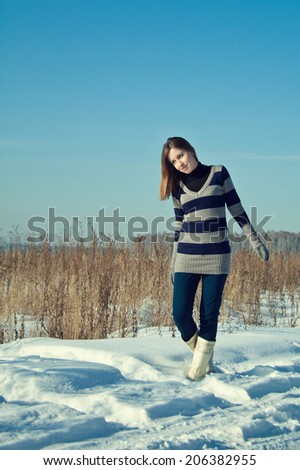 Young beautiful brunette girl in stripe sweater and white snow boots posing in the snow field