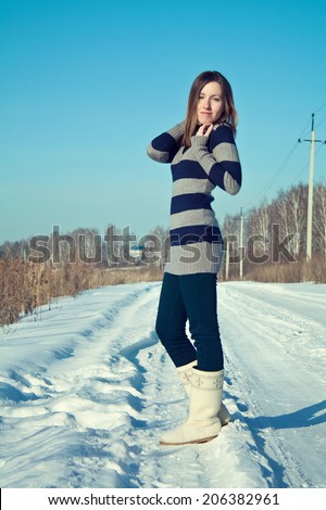 Young beautiful brunette girl in stripe sweater and white snow boots posing in the snow field