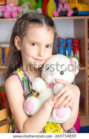 Girl 6 years brunette in colorful dress sitting on a chair holding a stuffed toy white bear