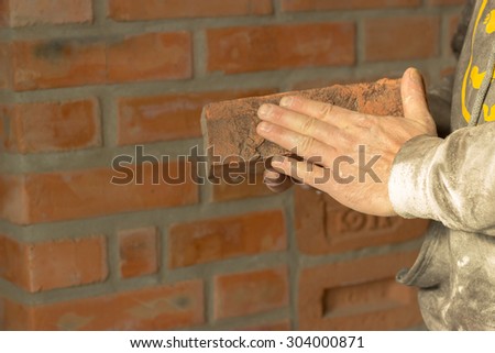 Men\'s hands are kept carved brick on brick wall background, man\'s hands are kept brick and hammer