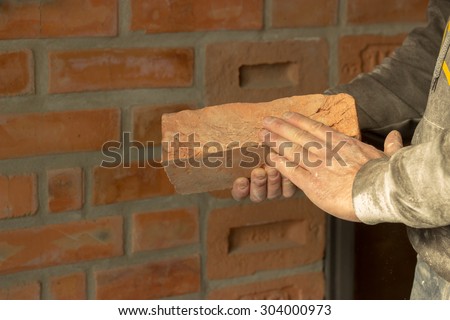Men\'s hands are kept carved brick on brick wall background, man\'s hands are kept brick and hammer