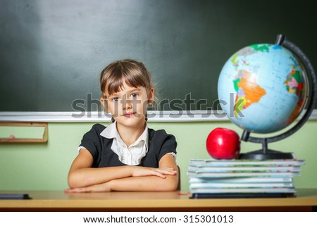 school, girl, schoolgirl 6 years in a black dress and a white shirt with two pigtails on the table Globe and red apple, microscope