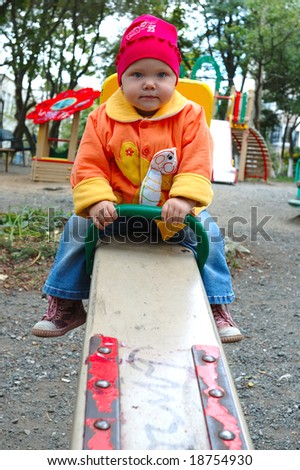 Pretty little girl with bright jacket sit on seesaw (teeter-totter).