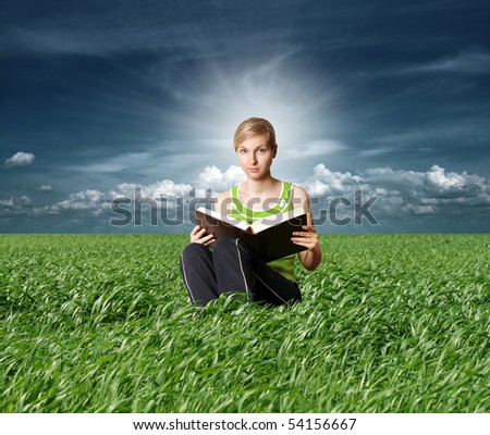 college girl reading big book in green grass